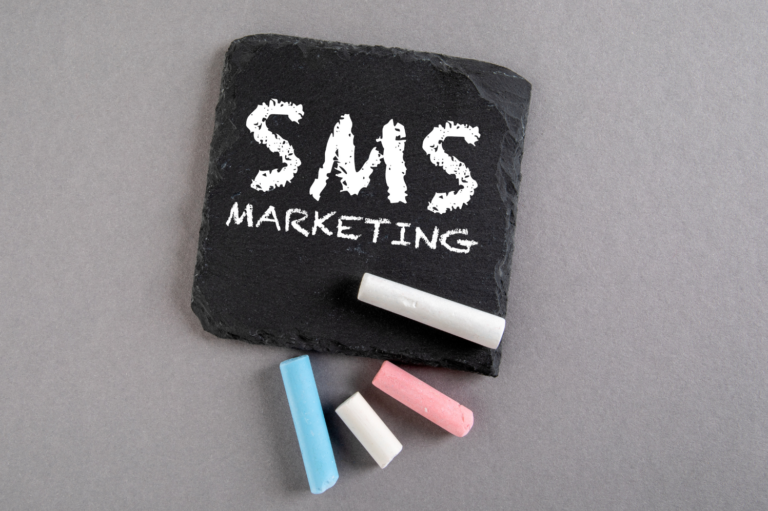 SMS marketing written on a chalkboard slate with colorful chalk sticks, representing tools for customer engagement through text message marketing.