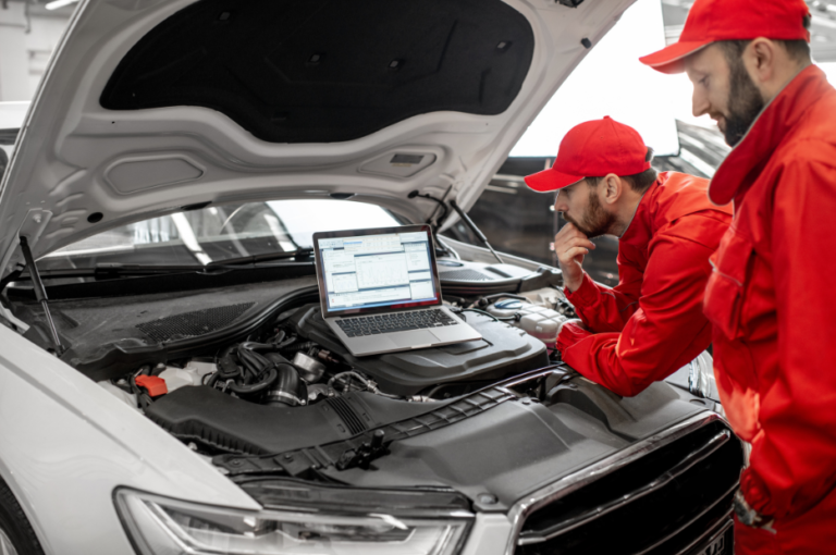 Mechanics using a laptop to diagnose a vehicle's engine in a modern automotive repair shop.