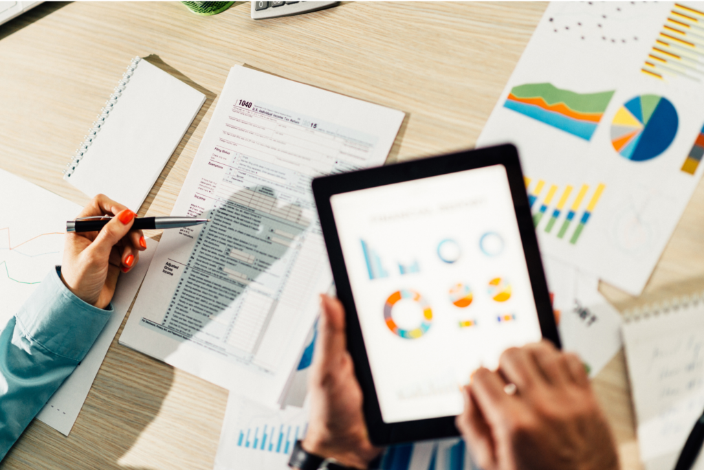 Person reviewing data charts and graphs on a tablet and paper, ensuring consistency of business information across platforms.