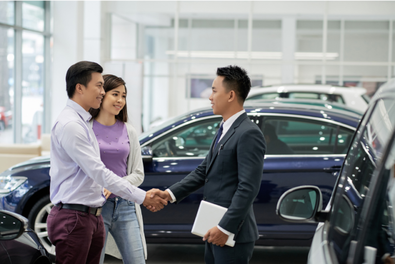 Car salesperson shaking hands with a couple at an automotive dealership, sealing a deal.