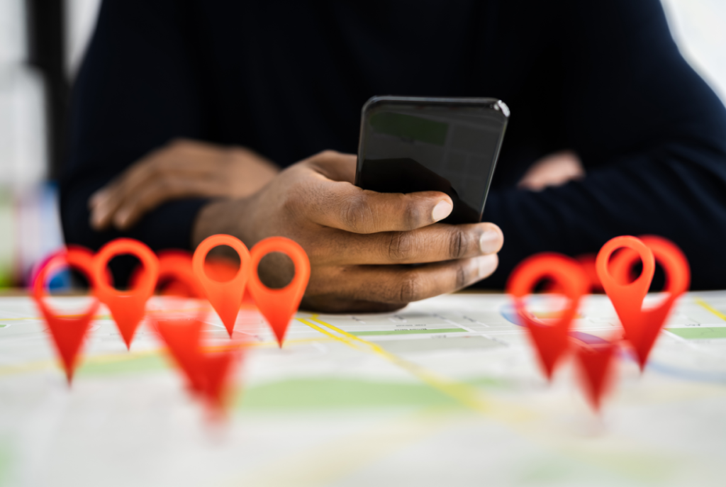 A person holds a smartphone over a map with several red location pins, representing local search and SEO optimization for businesses.