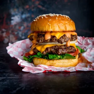 A delicious double cheeseburger with melted cheese, lettuce, tomato, and sauce, served on a sesame seed bun.